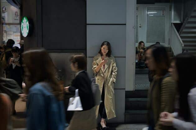 ragazza giapponese guarda il telefono appoggiata al muro in stazione